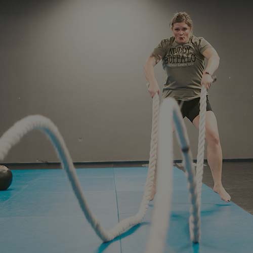 Woman using battle ropes on workout mat during strength and conditioning class at American Top Team Gym in Watertown, NY