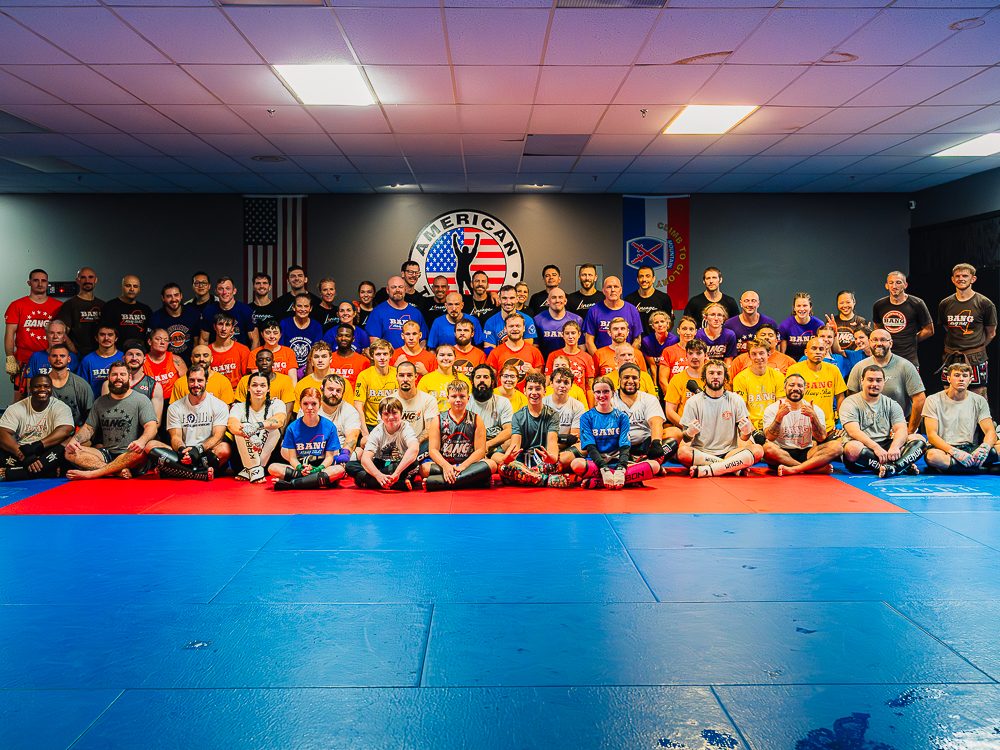 Full team group photo at American Top Team Watertown: adults, teens, and kids in BANG Muay Thai shirts on the mats