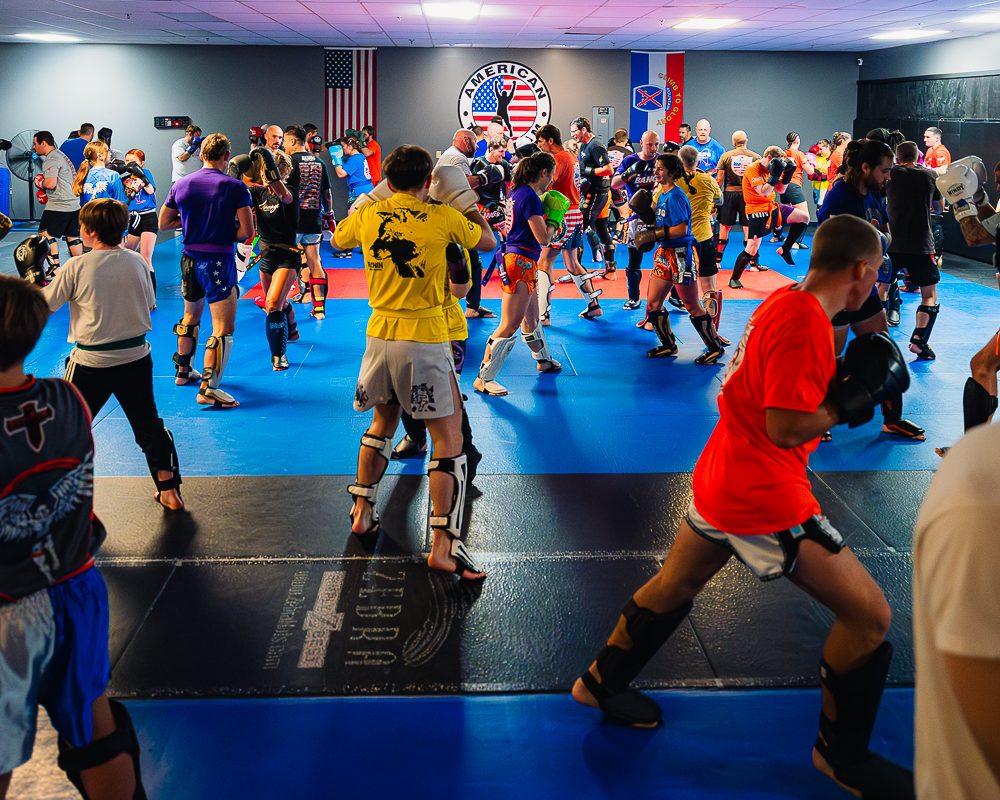 Packed BANG Muay Thai class doing partner pad work at American Top Team Watertown, with adults, teens, and kids training together