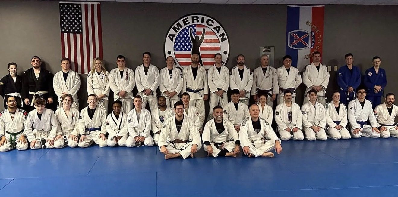 Brazilian Jiu-Jitsu class group photo at American Top Team Watertown, with US flag and 10th Mountain Division flag visible in the background